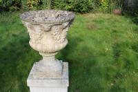 A pair of composite stone urns on plinths